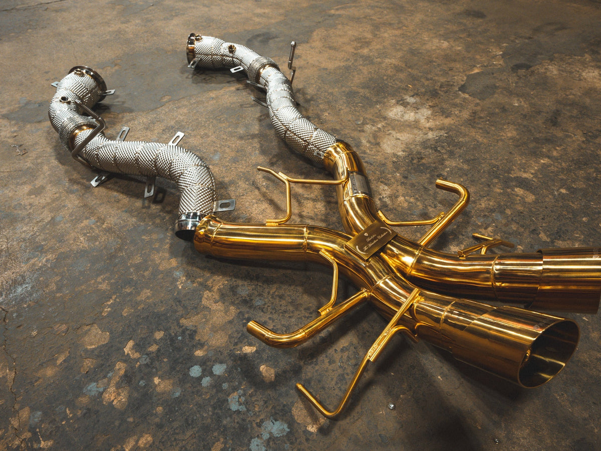 Mclaren P1 Sport Exhaust System with polished gold-toned titanium pipes, silver heat-wrapped sections, and wide twin tips.