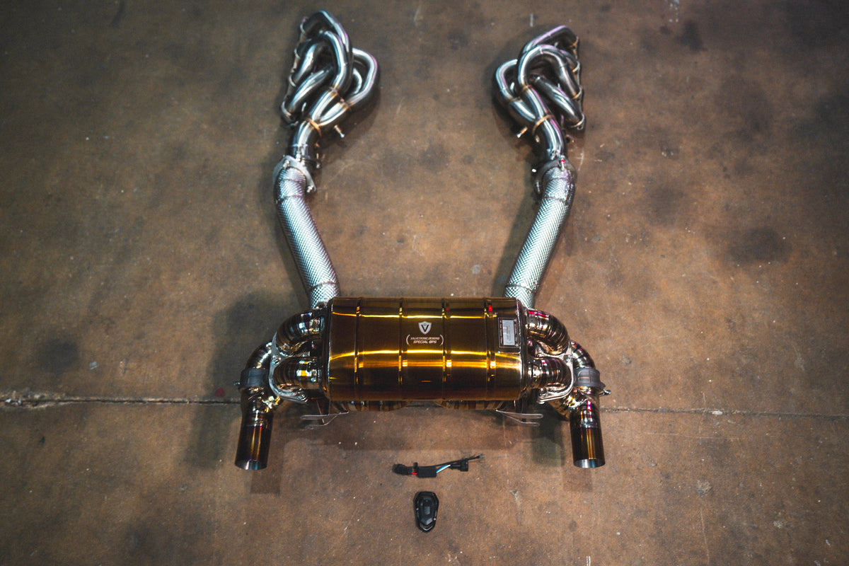 Ferrari F430 Scuderia valved sport exhaust system in polished stainless steel with a gold-toned muffler and twin pipes.