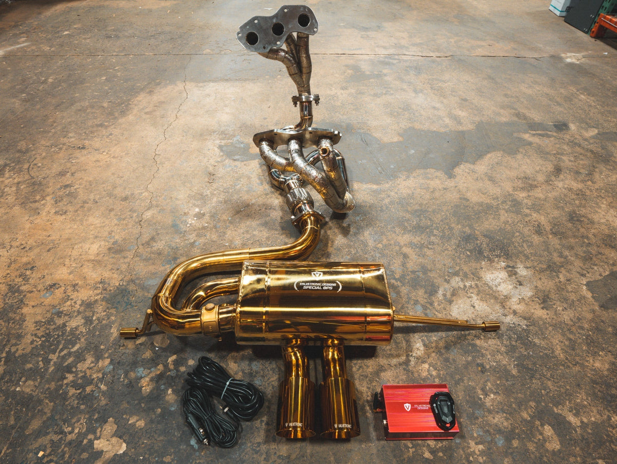 Lotus Evora Valved Sport Exhaust System with gold-toned metal tubing, polished muffler, welded headers, and valve controls.
