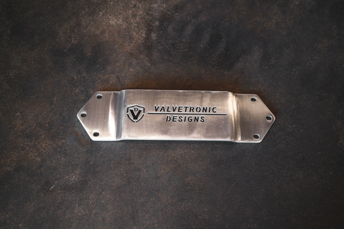 Chassis brace for BMW F80/F82/F83/F87C in brushed silver metal, with angled ends, mounting holes and engraved logo.