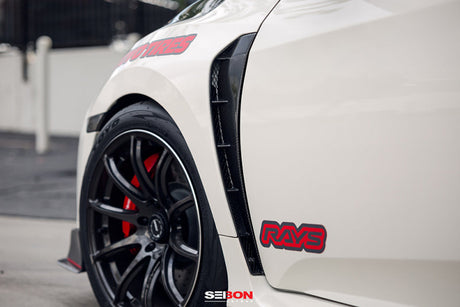 Close-up of Seibon 17-18 Honda Civic Type-R carbon fiber fender duct on white car with black wheel and red brake caliper